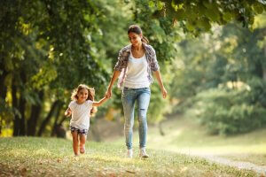 mother and daughter walking in a park while holding her hands