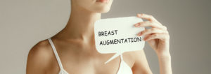 woman holding a piece of paper with breast augmentation written on it